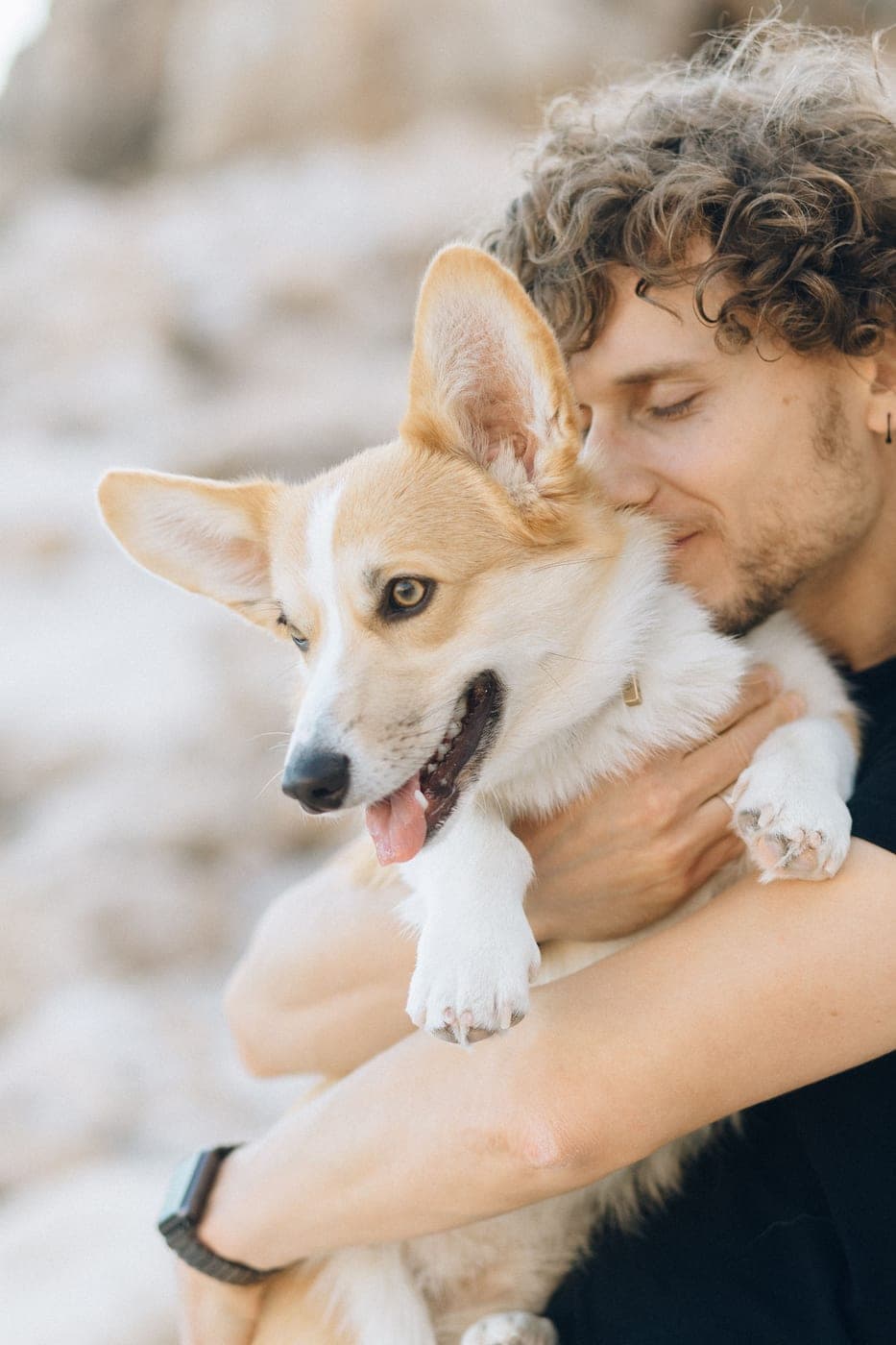 A man hugging a happy corgi